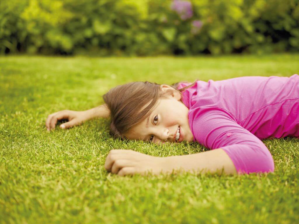Mädchen liegt auf dem Rasen und guckt in die Kamera