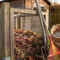 Drahtkorb aus Pfählen gefüllt mit Herbstlaub, daneben Mistgabel und Laubbesen für das Laub im Garten